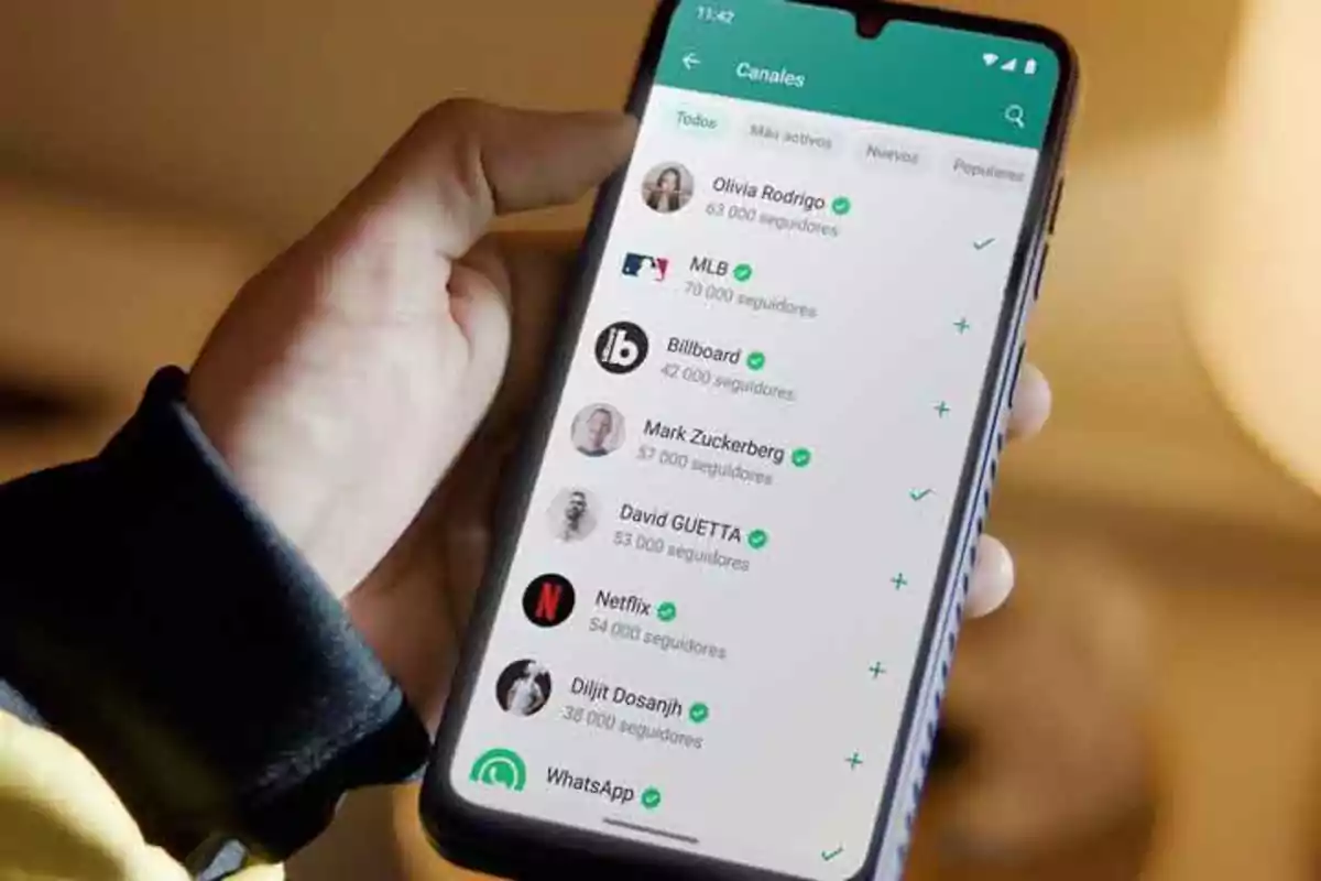 Una mano sosteniendo un teléfono móvil que muestra una lista de canales en una aplicación de mensajería.