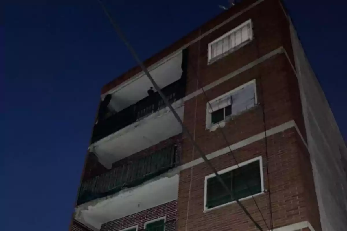 Edificio de ladrillo de cuatro pisos con balcones y ventanas, visto desde abajo en la noche.