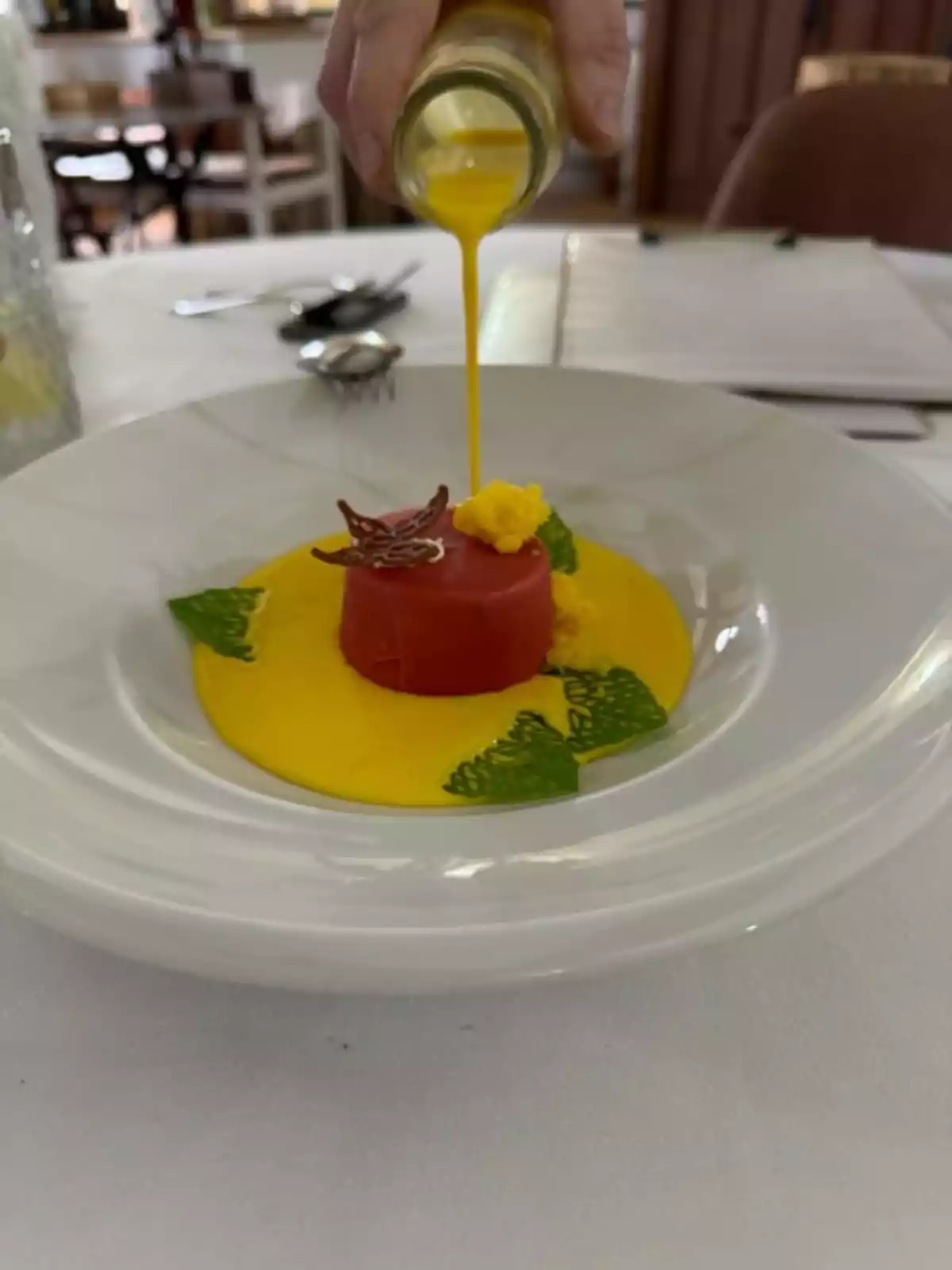 Una mano vertiendo una salsa amarilla sobre un plato con una presentación gourmet en un restaurante.