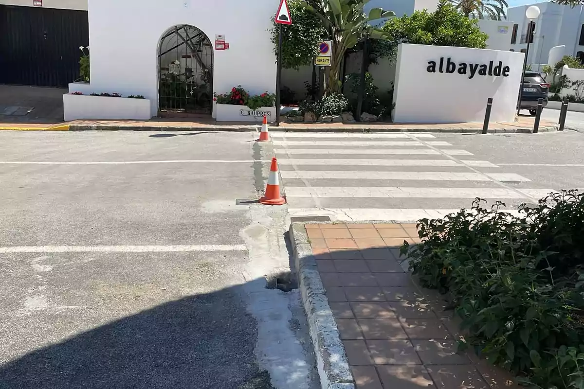 Una calle con un paso de peatones y conos naranjas, junto a un edificio blanco con el letrero 