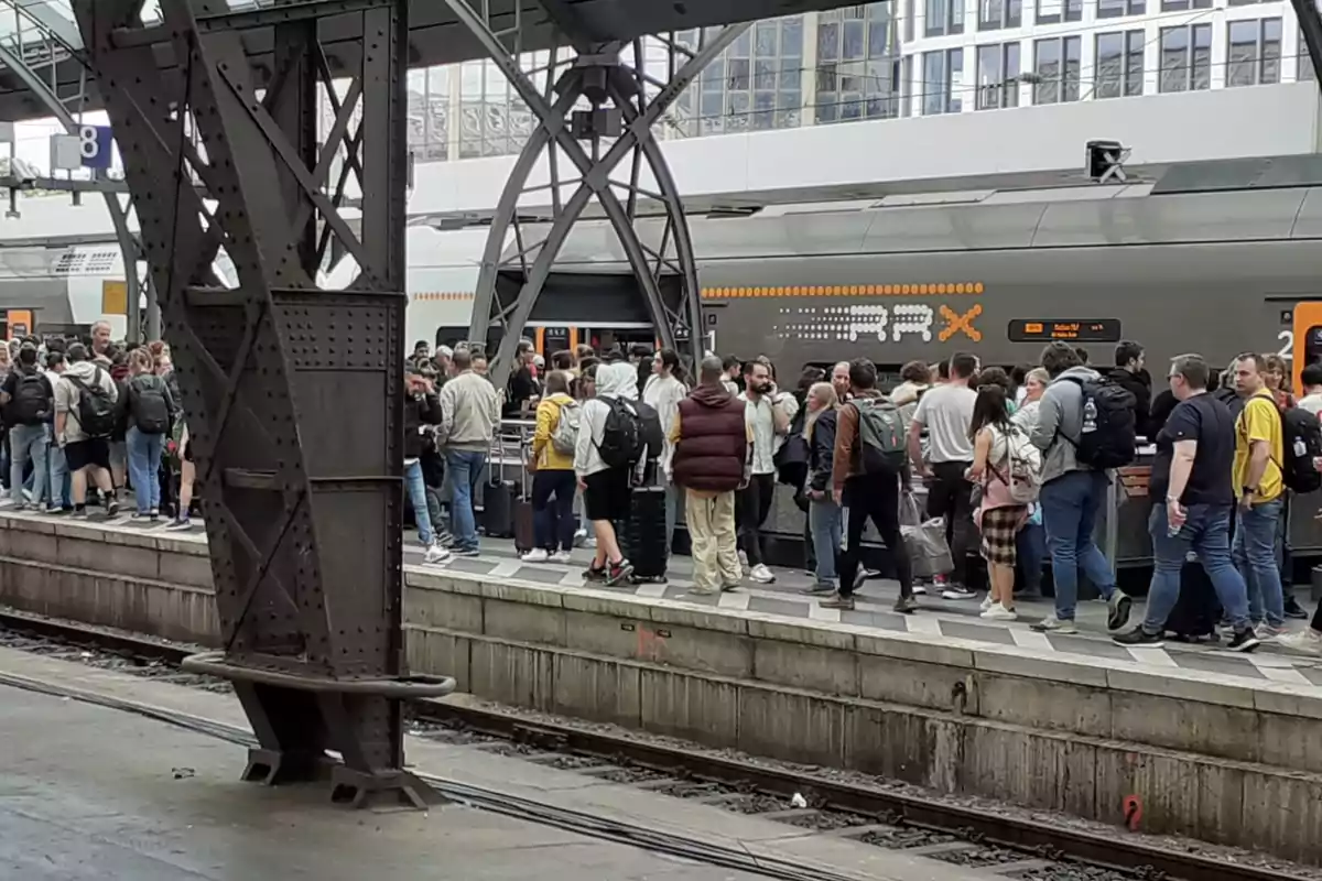 Una multitud de personas espera en el andén de una estación de tren mientras un tren está detenido.