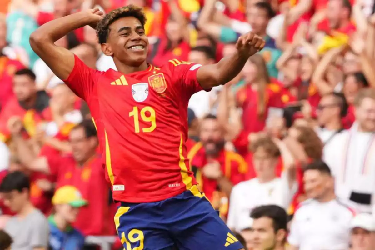 Jugador de fútbol celebrando un gol con la camiseta de la selección española, rodeado de aficionados en las gradas.