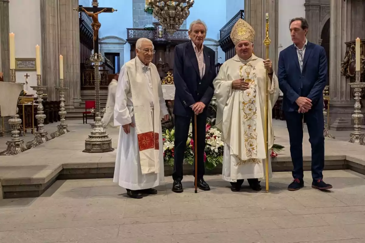 Cuatro hombres posan en el interior de una iglesia, dos de ellos con vestimenta religiosa y los otros dos con trajes formales.