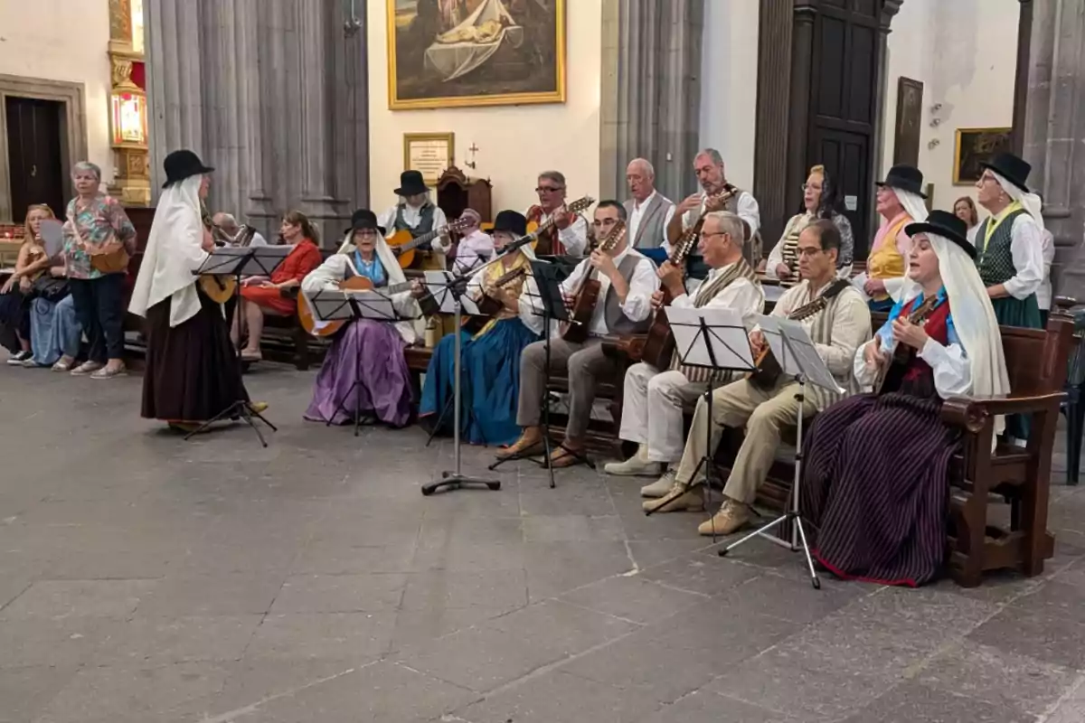 Un grupo de personas vestidas con trajes tradicionales está tocando instrumentos musicales y cantando en el interior de una iglesia, mientras otras personas observan desde los bancos.