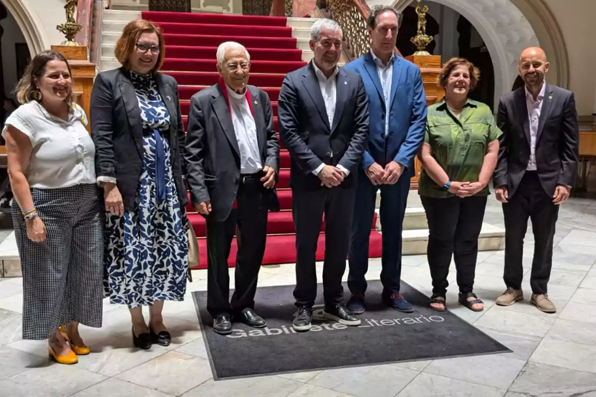 Un grupo de personas posando en un edificio con una alfombra que dice "Gabinete Literario" y una escalera con alfombra roja al fondo.