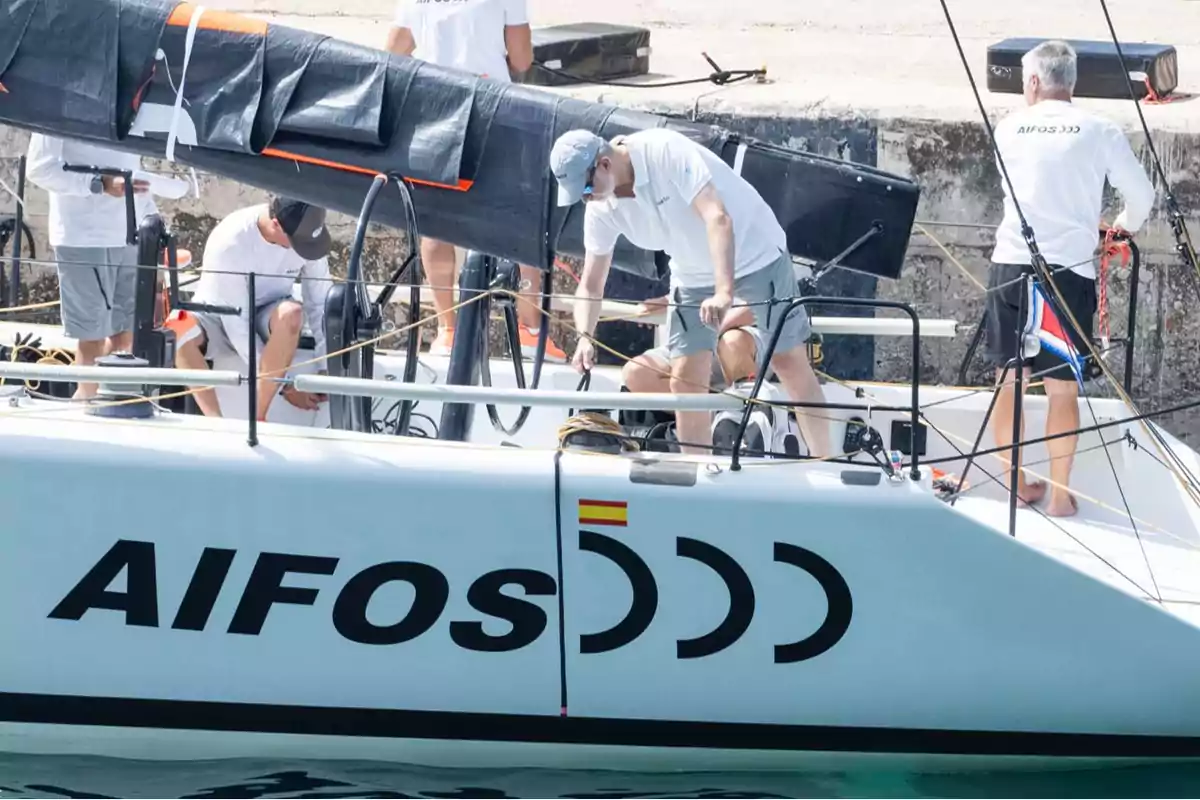 Personas trabajando en un velero llamado Aifos 333 en un puerto.