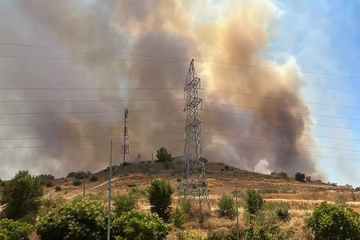 Incendio forestal en una colina con torres de transmisión eléctrica y antenas de telecomunicaciones.