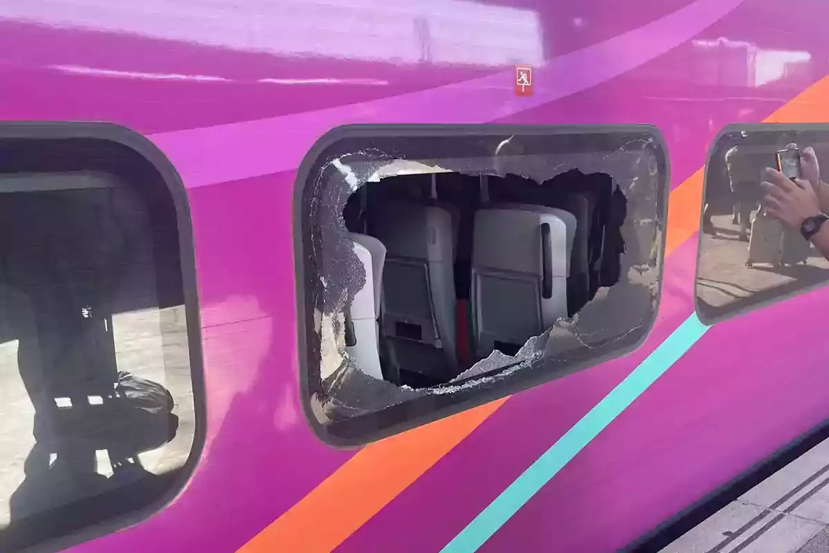 Ventana rota de un tren de color morado con asientos visibles en el interior.