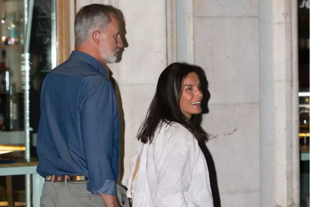 Una pareja caminando juntos, el hombre con camisa azul y la mujer con blusa blanca, ambos parecen estar disfrutando de la noche.