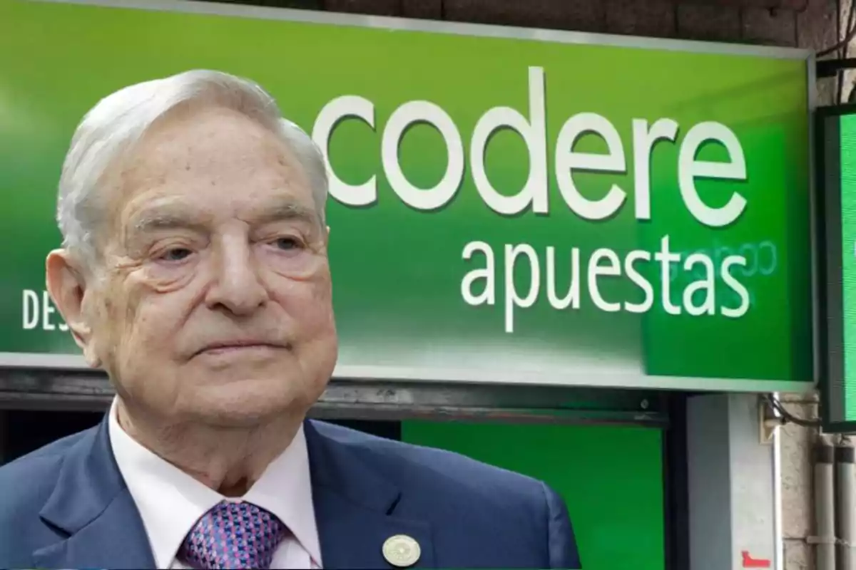 Un hombre mayor con cabello canoso y traje formal está frente a un letrero verde que dice "codere apuestas".