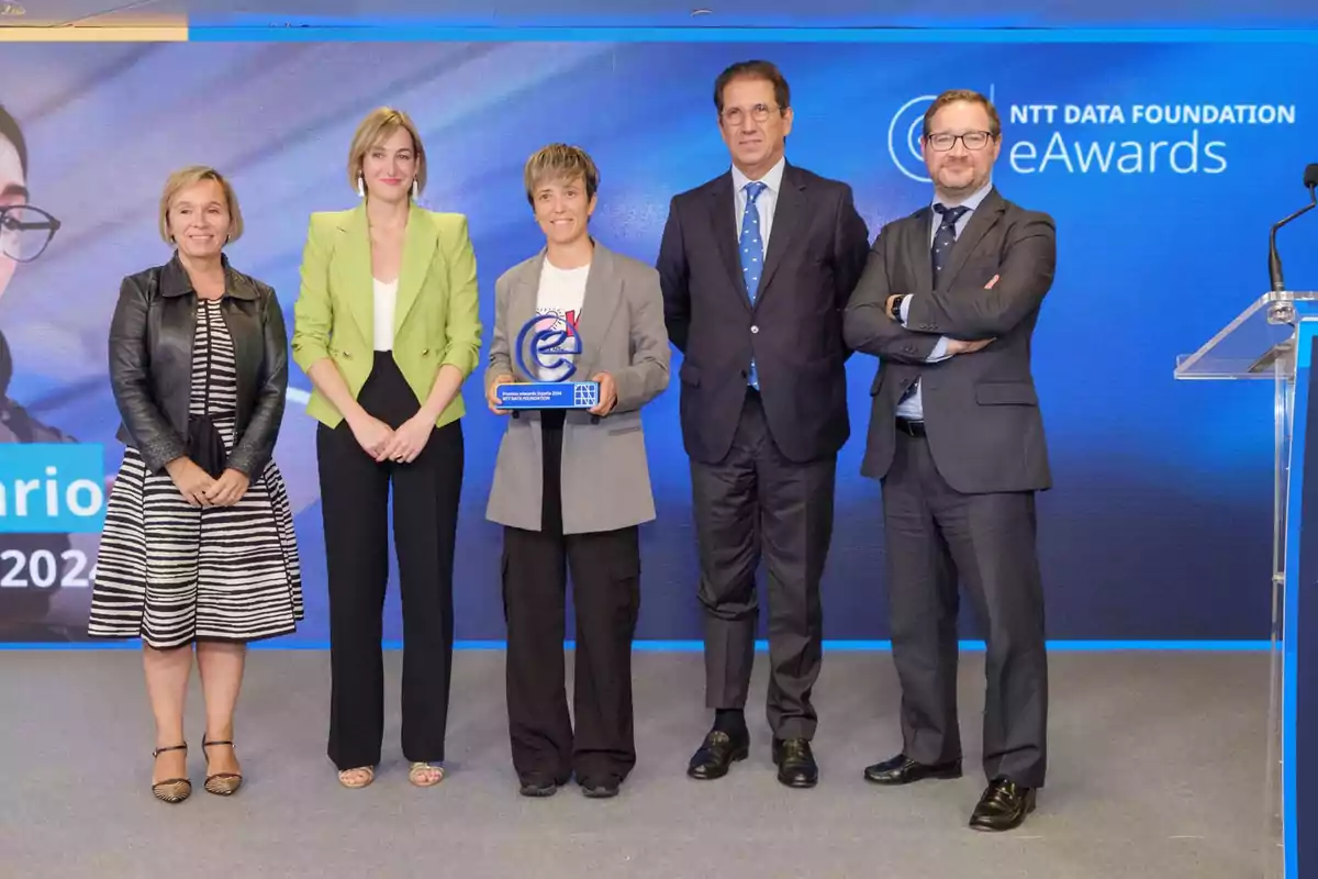 Cinco personas posan en un escenario durante una ceremonia de premiación, una de ellas sostiene un trofeo azul.