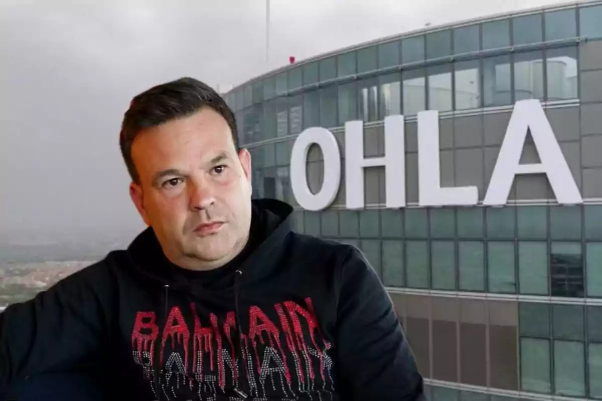 Un hombre con sudadera negra y letras rojas está sentado frente a un edificio de cristal con el letrero "OHLA".