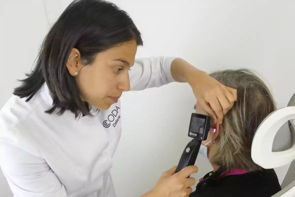 Una profesional de la salud realiza un examen auditivo a una persona usando un otoscopio.