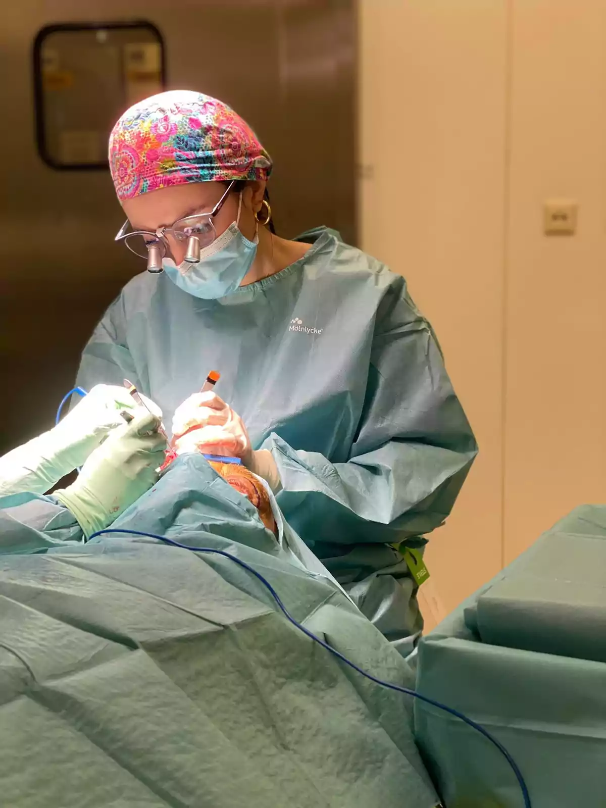 Una cirujana con gorro colorido y mascarilla realiza una operación en un quirófano.