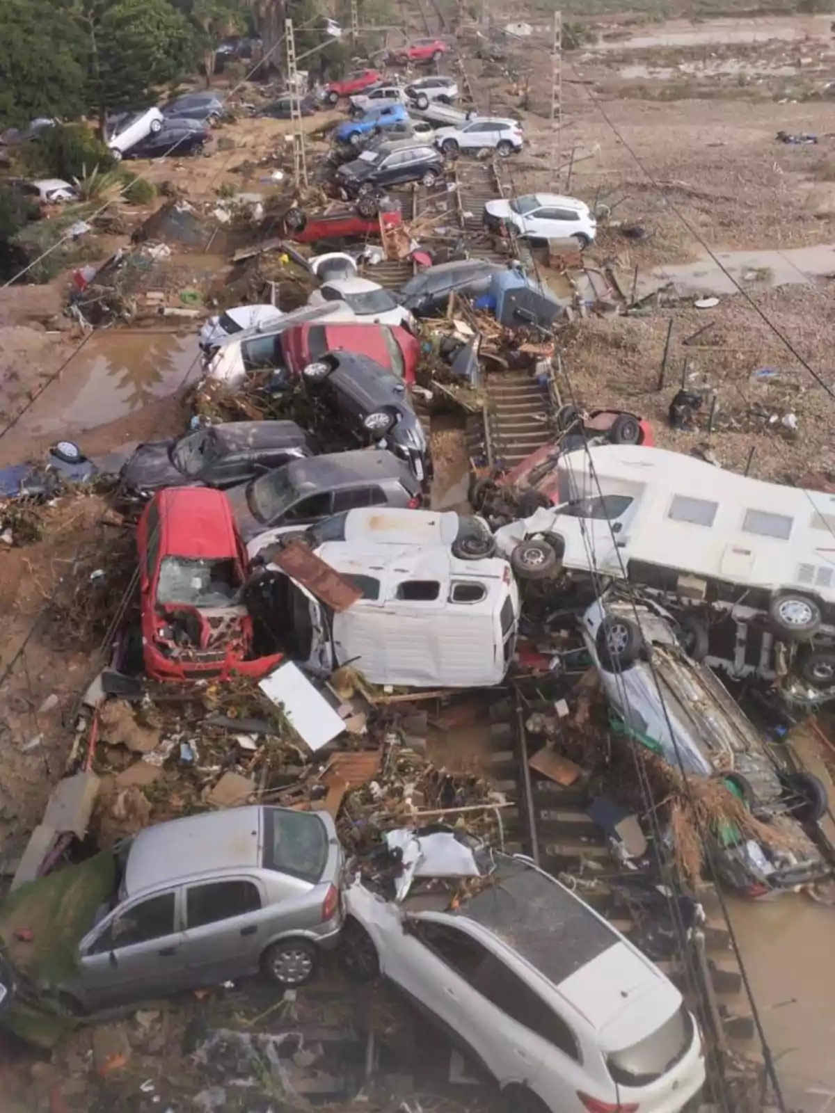 Una escena de varios coches apilados y dañados en una zona afectada por una inundación.