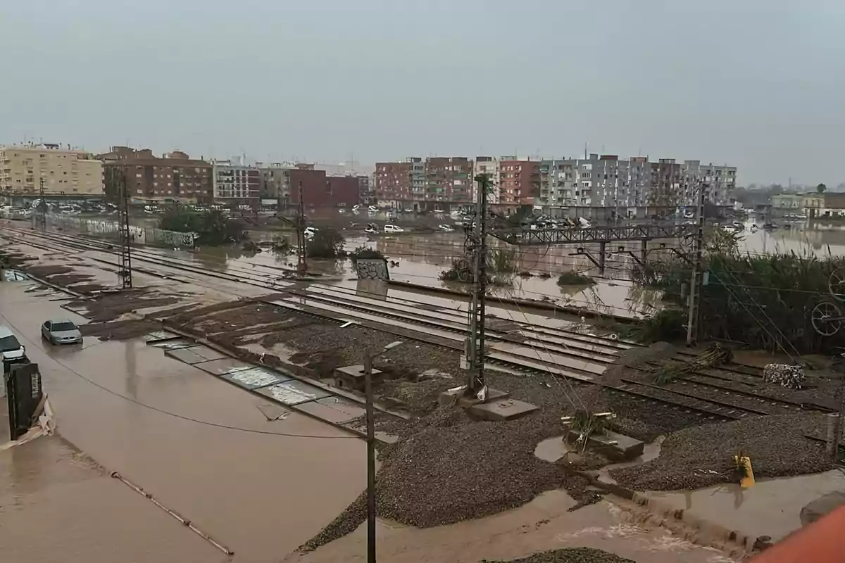 Inundación en una zona urbana con vías de tren cubiertas de agua y edificios al fondo.