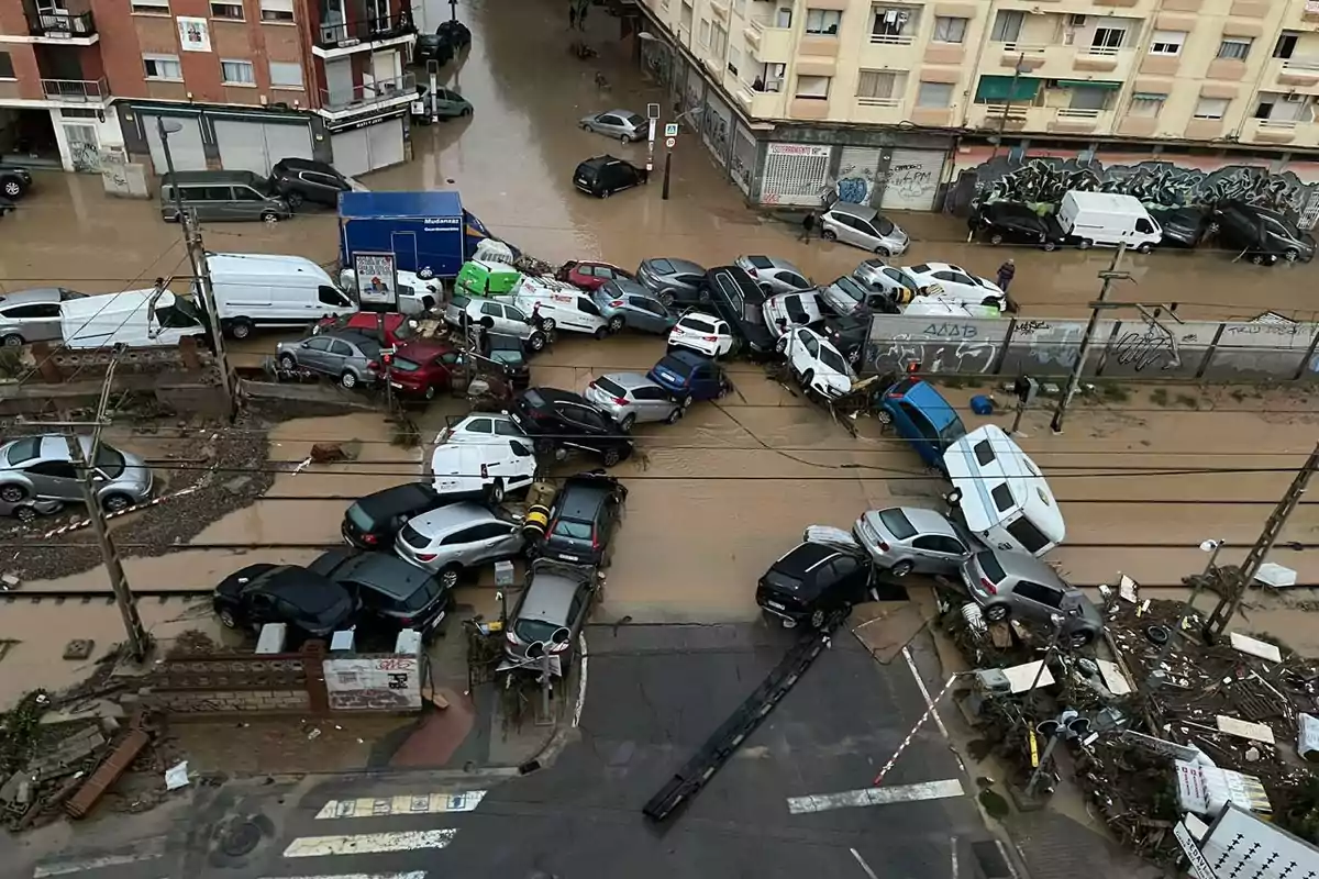 Una calle inundada con numerosos vehículos amontonados y dañados debido a la acumulación de agua y escombros.