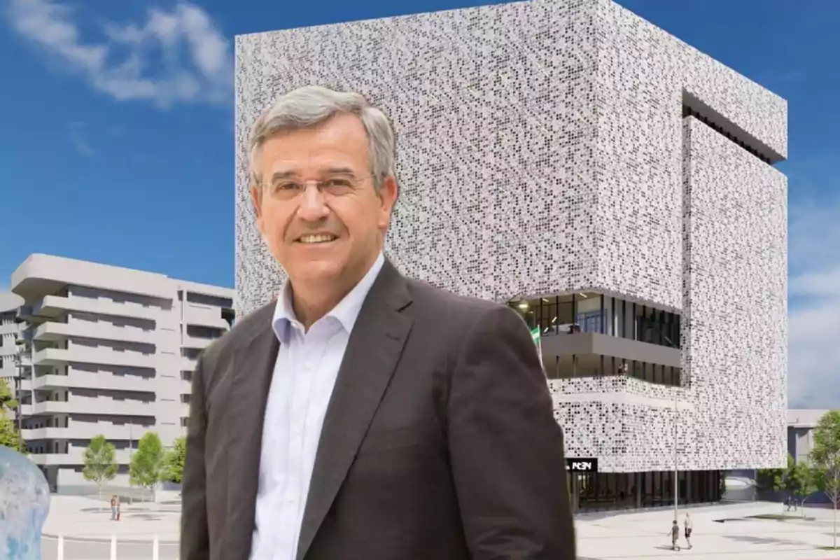 Un hombre de traje sonríe frente a un edificio moderno con fachada de diseño geométrico.