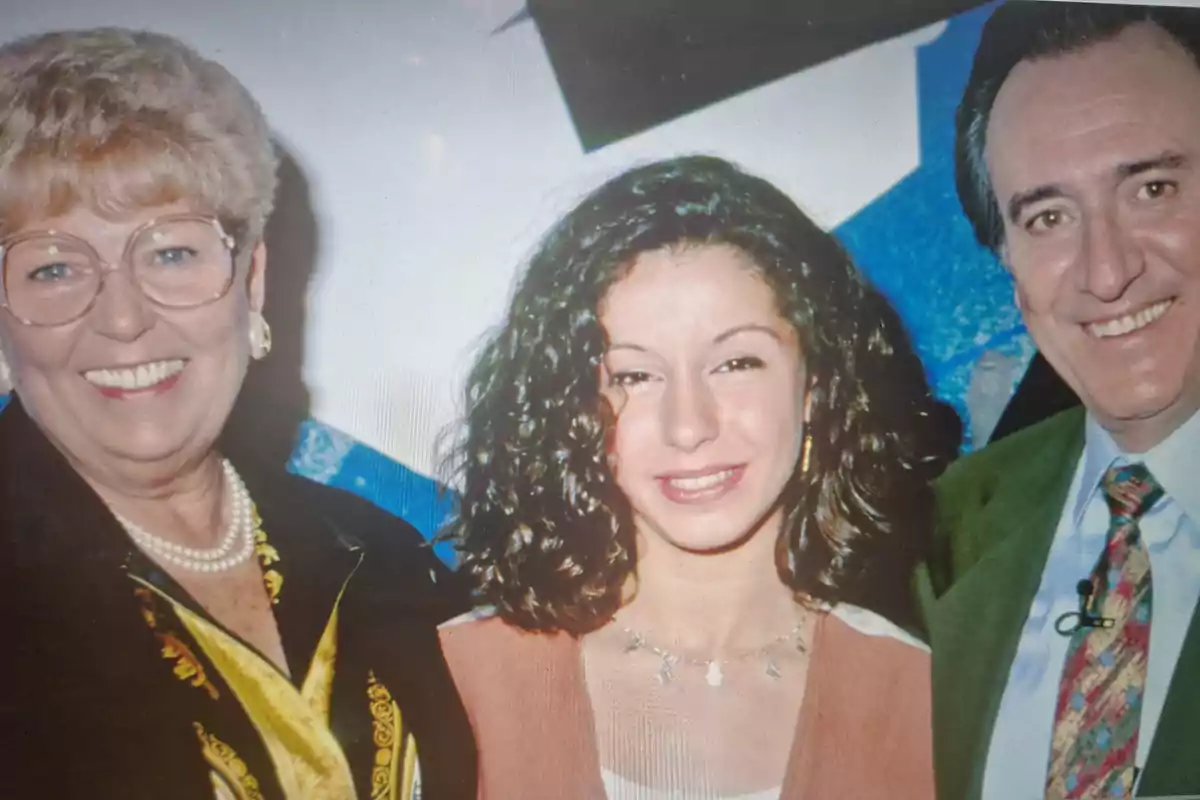 Tres personas sonrientes posan juntas frente a un fondo azul y blanco.