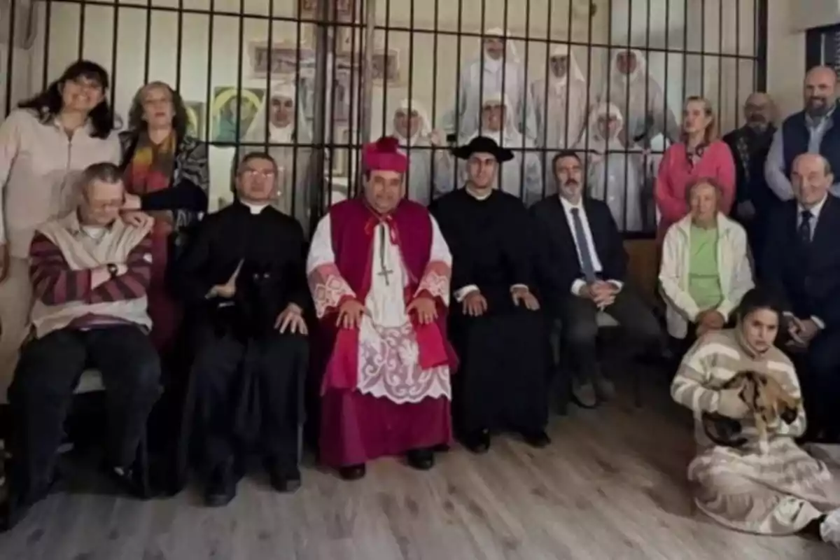 Un grupo de personas, incluyendo clérigos y monjas, posan para una foto en una habitación con rejas al fondo.