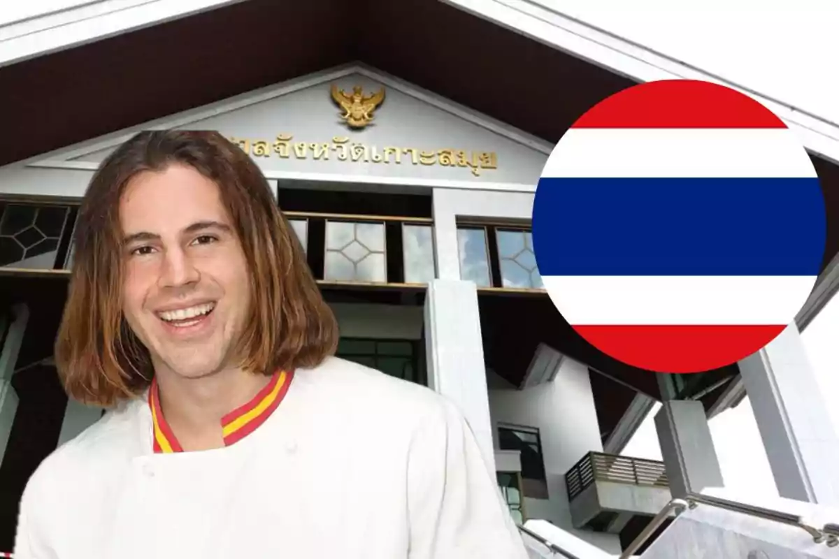 Un hombre sonriente con cabello largo y una chaqueta blanca frente a un edificio con arquitectura moderna y un emblema dorado, junto a un círculo con los colores de la bandera de Tailandia.