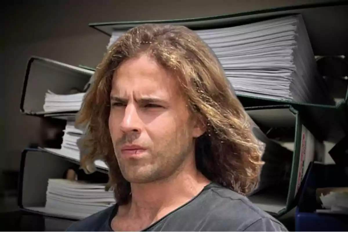 Un hombre de cabello largo y castaño está frente a un fondo de archivadores llenos de documentos.