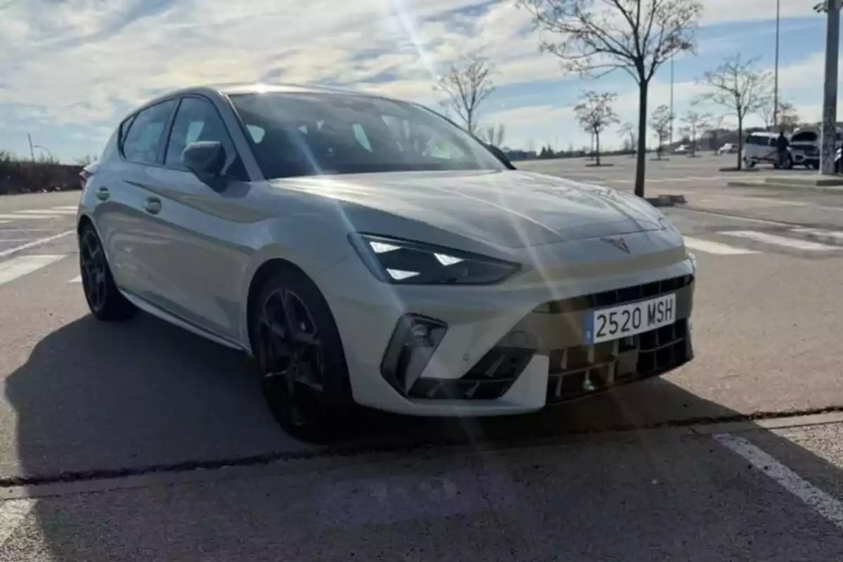 Un CUPRA León 1.5 TSI blanco estacionado en un aparcamiento bajo un cielo parcialmente nublado.