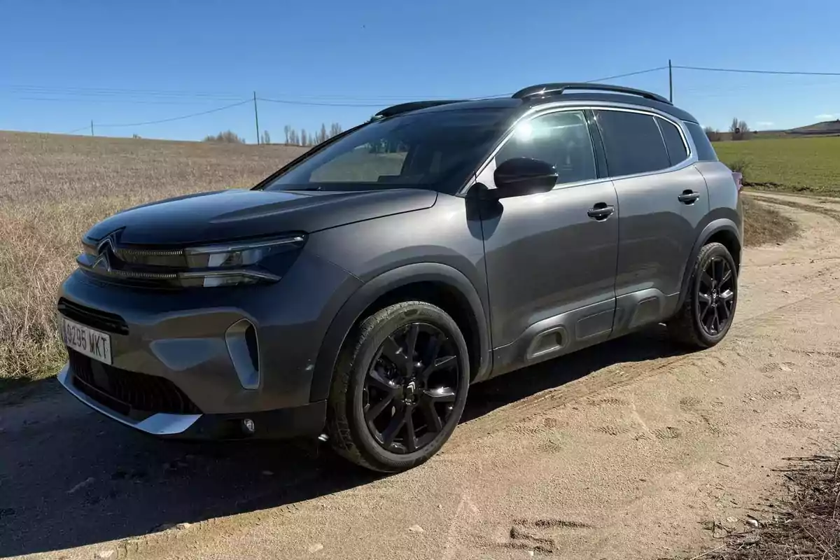 Un SUV gris estacionado en un camino de tierra con un paisaje rural de fondo y un cielo despejado.