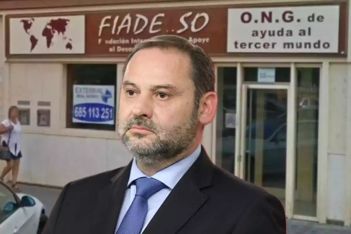 Un hombre con traje y corbata está frente a un edificio que tiene un cartel de una ONG de ayuda al tercer mundo.