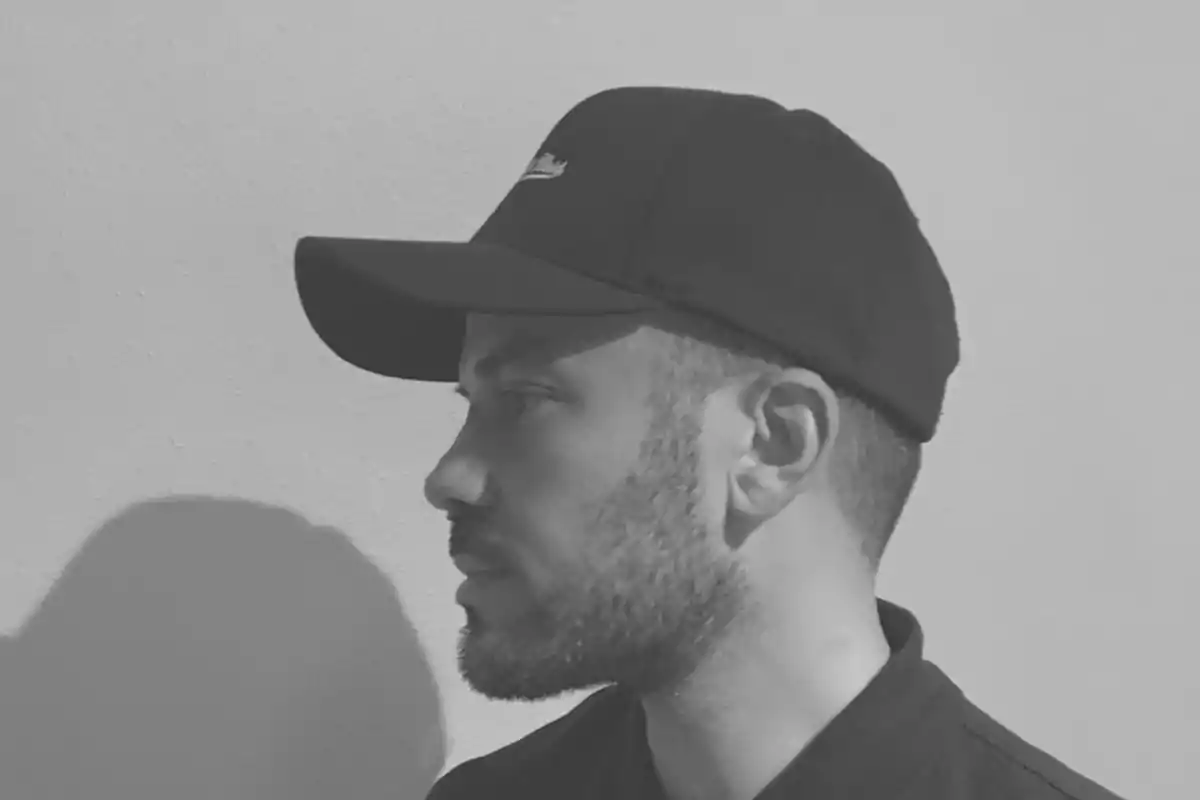 Hombre de perfil con gorra negra mirando hacia la derecha en una imagen en blanco y negro.