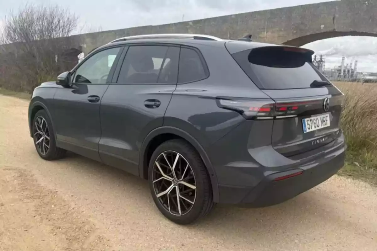 Un Volkswagen Tiguan eTSI gris estacionado en un camino de tierra con un puente de fondo.