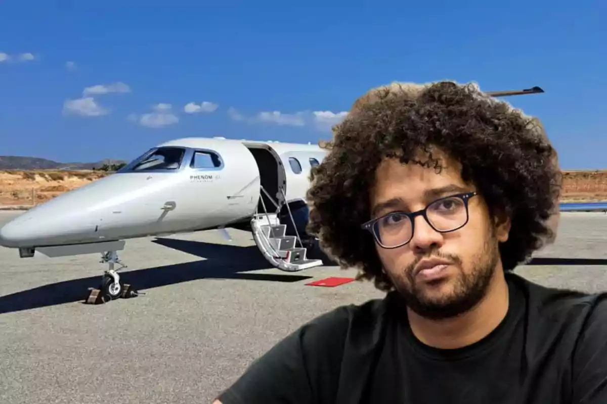 Un hombre con gafas y cabello rizado está frente a un avión privado en una pista de aterrizaje bajo un cielo despejado.