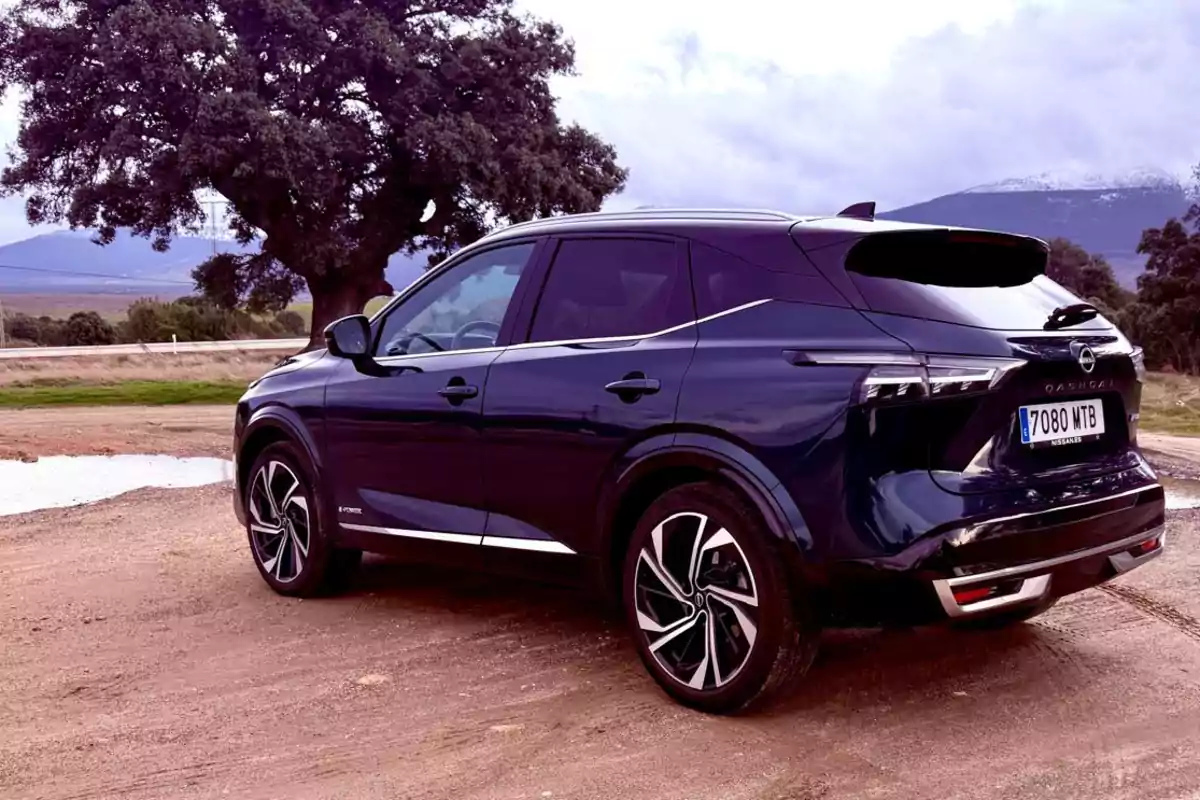 Un Nissan Qashqai e-POWER 2025 negro estacionado en un camino de tierra con un árbol grande y montañas al fondo. Un Nissan Qashqai e-POWER 2025 negro estacionado en un camino de tierra con un árbol grande y montañas al fondo.