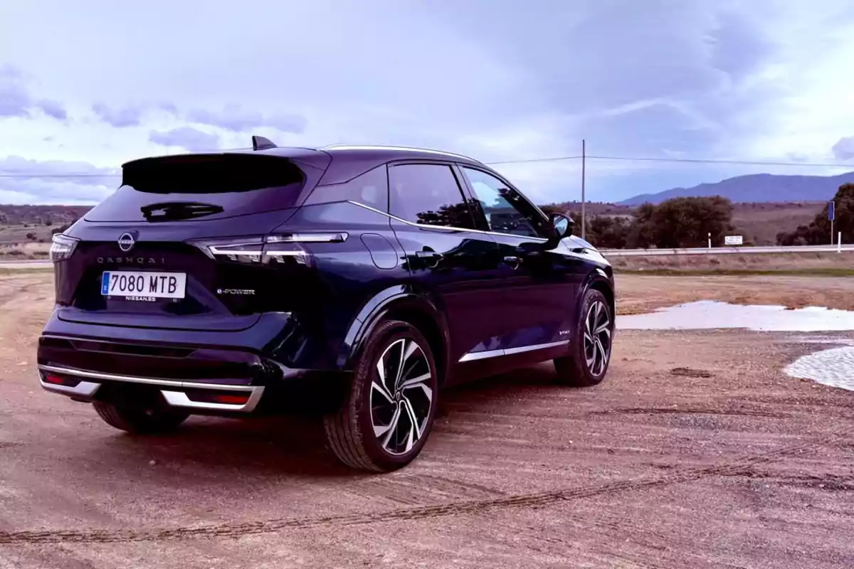 Un Nissan Qashqai e-POWER 2025 negro estacionado en un camino de tierra con un paisaje montañoso al fondo.