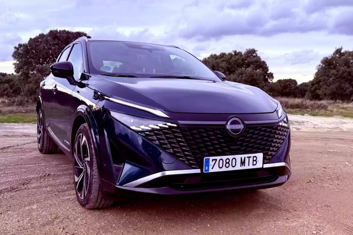 Un coche Nissan Qashqai e-POWER 2025 oscuro estacionado en un camino de tierra con árboles y un cielo nublado al fondo. Un coche Nissan Qashqai e-POWER 2025 oscuro estacionado en un camino de tierra con árboles y un cielo nublado al fondo.