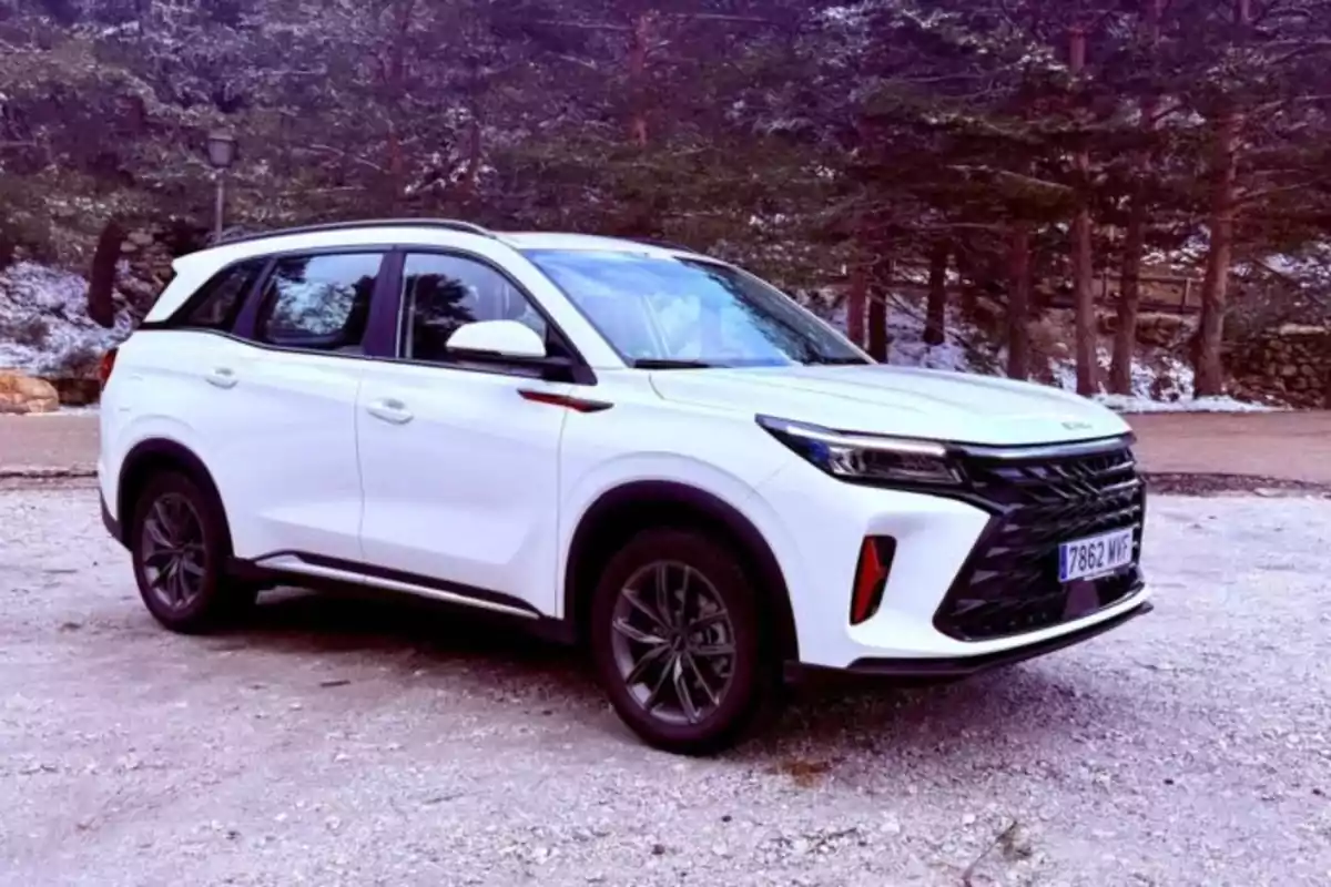 Un DFSK Fengon 600 blanco estacionado en un camino de tierra con árboles al fondo.