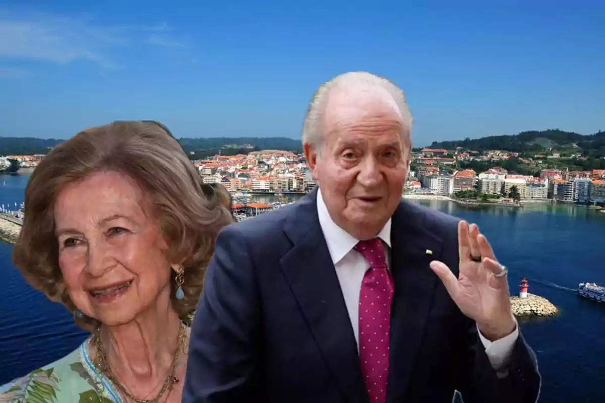 Dos personas mayores posan frente a un paisaje costero con edificios y un faro.
