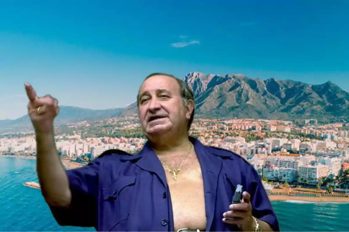Un hombre con camisa abierta y cadena dorada gesticula con la mano frente a un paisaje urbano y montañoso.