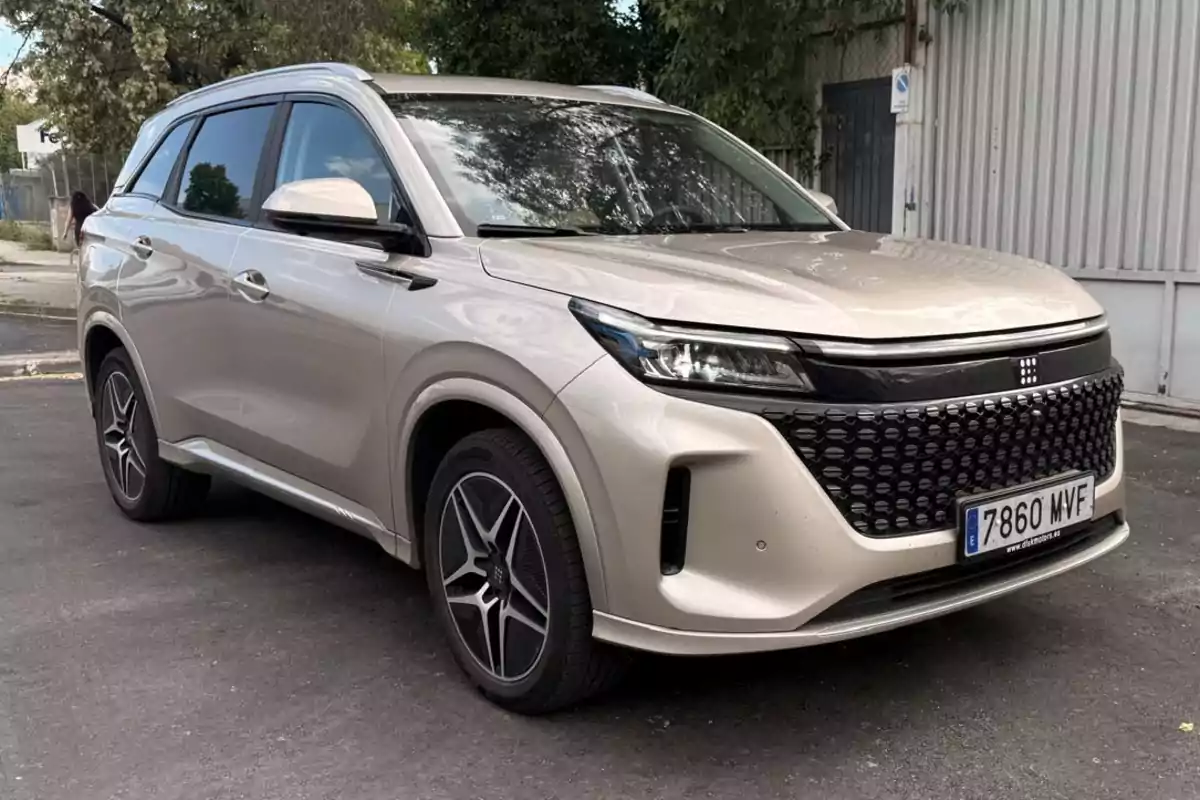 Un DFSK E5 de color beige estacionado en una calle, con un diseño elegante y una matrícula visible en la parte delantera.