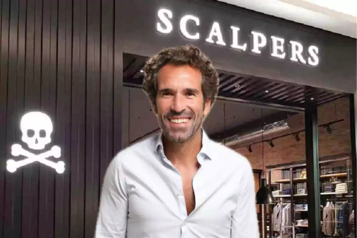 Un hombre sonriente con camisa blanca frente a una tienda de ropa con el letrero "Scalpers" y un logotipo de calavera y huesos cruzados.
