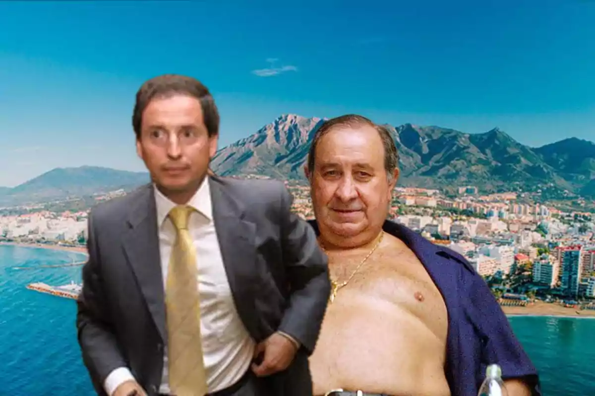 Dos hombres en primer plano, uno con traje y corbata y el otro con el pecho descubierto y una cadena dorada, posan frente a un paisaje costero con montañas y edificios al fondo.