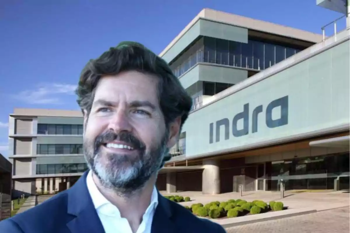Hombre sonriente con barba frente a un edificio moderno con el logo de Indra