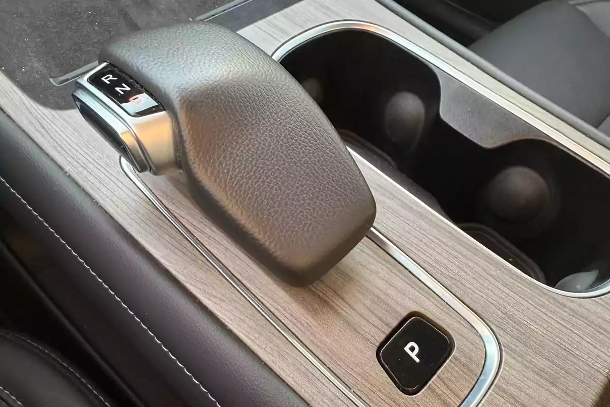 Palanca de cambios automática de un automóvil sobre una consola central con acabado tipo madera y portavasos. Palanca de cambios automática de un automóvil sobre una consola central con acabado tipo madera y portavasos.