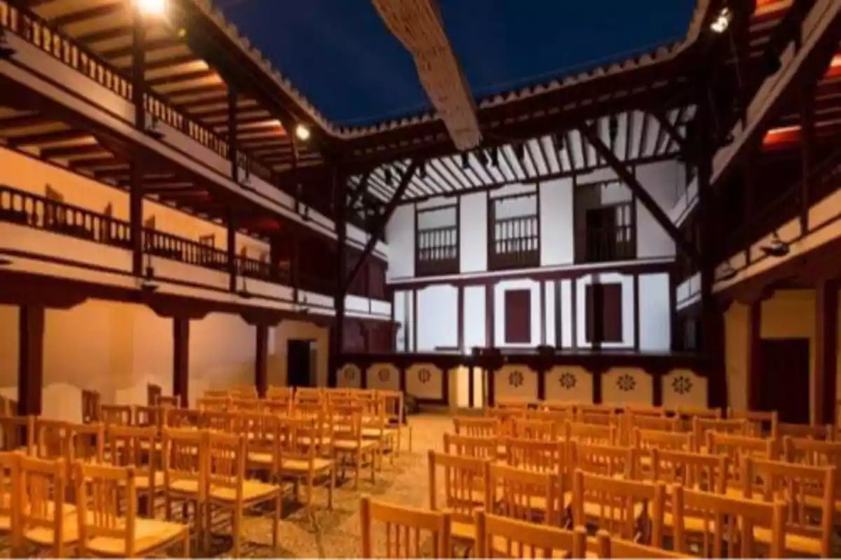 Patio de un teatro antiguo con sillas de madera alineadas y balcones de madera alrededor
