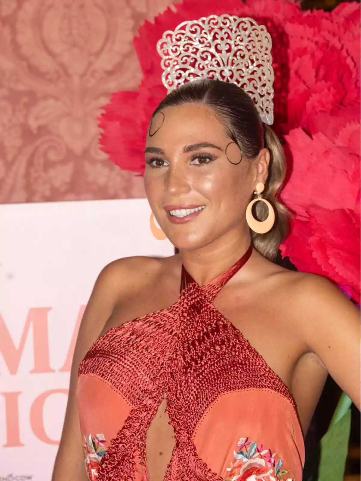 Mujer sonriente con vestido rojo y tocado tradicional adornado, posando frente a un fondo decorativo Mujer sonriente con vestido rojo y tocado tradicional adornado, posando frente a un fondo decorativo