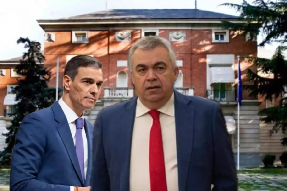 Dos hombres con traje posan frente a un edificio de ladrillo rojo con banderas y árboles alrededor