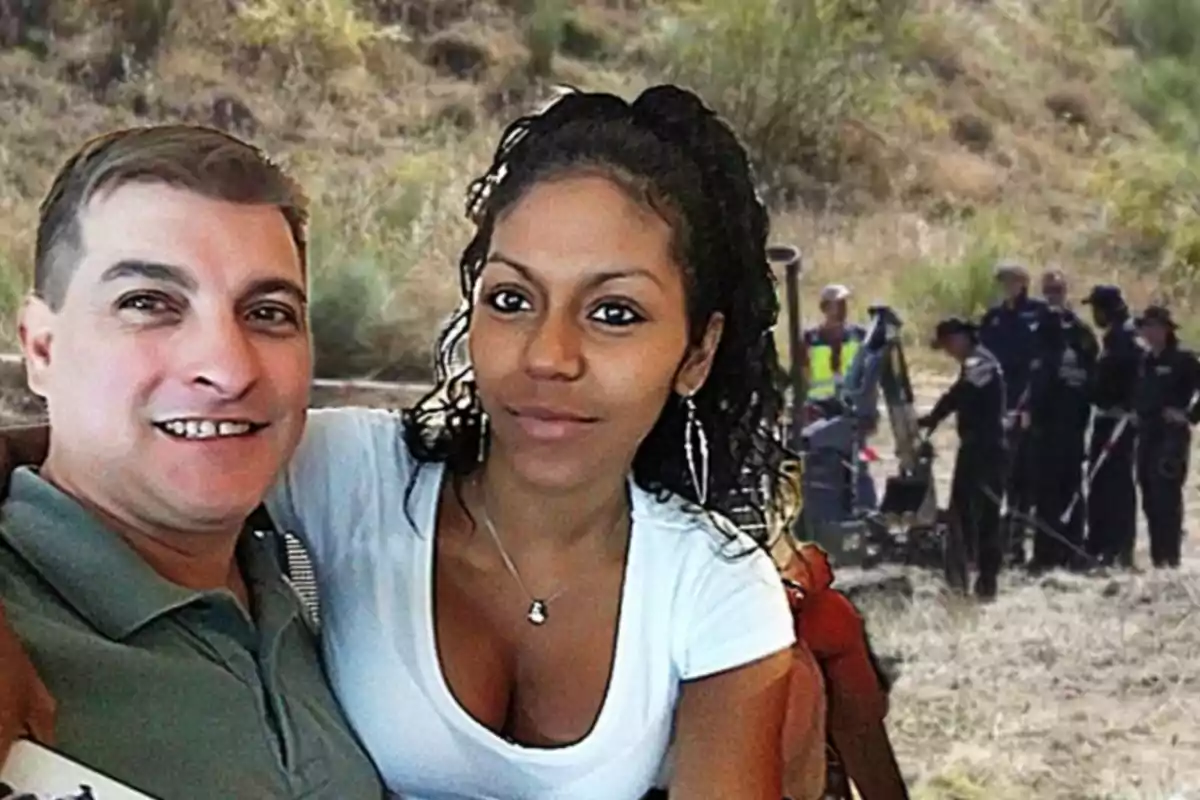 Una pareja se toma una selfie mientras al fondo se observa a un grupo de personas trabajando en un área al aire libre con vegetación.