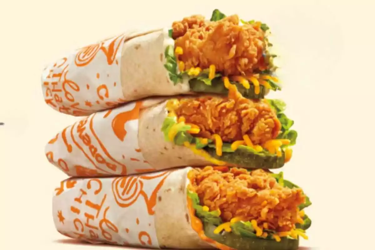 Three burritos wrapped in paper with breaded chicken, lettuce, and shredded cheese Three burritos wrapped in paper with breaded chicken, lettuce, and shredded cheese