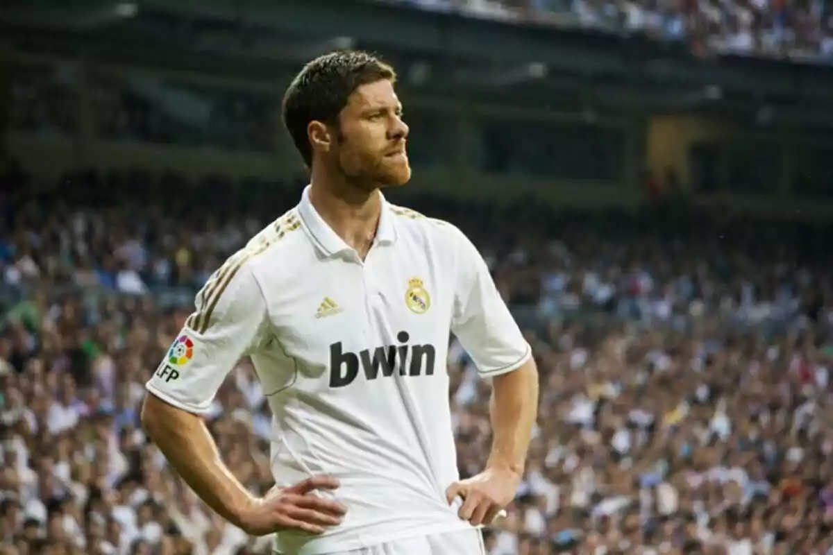 Futbolista del Real Madrid con uniforme blanco en el campo durante un partido, con las manos en la cintura y el estadio lleno de aficionados al fondo Futbolista del Real Madrid con uniforme blanco en el campo durante un partido, con las manos en la cintura y el estadio lleno de aficionados al fondo