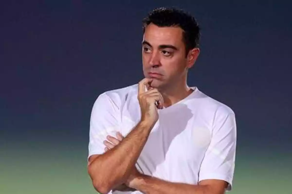 Hombre con camiseta blanca en pose pensativa con la mano en la barbilla y el brazo cruzado.
